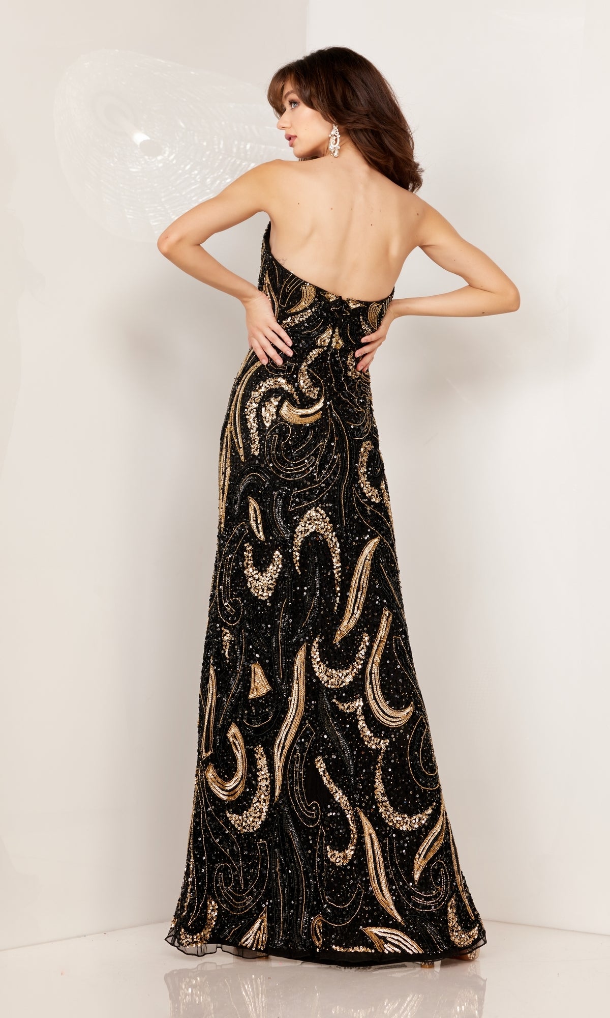 A woman faces away, wearing the Strapless Sequin-Print Long Prom Dress 1105 with gold and silver patterns, set against a plain light background.